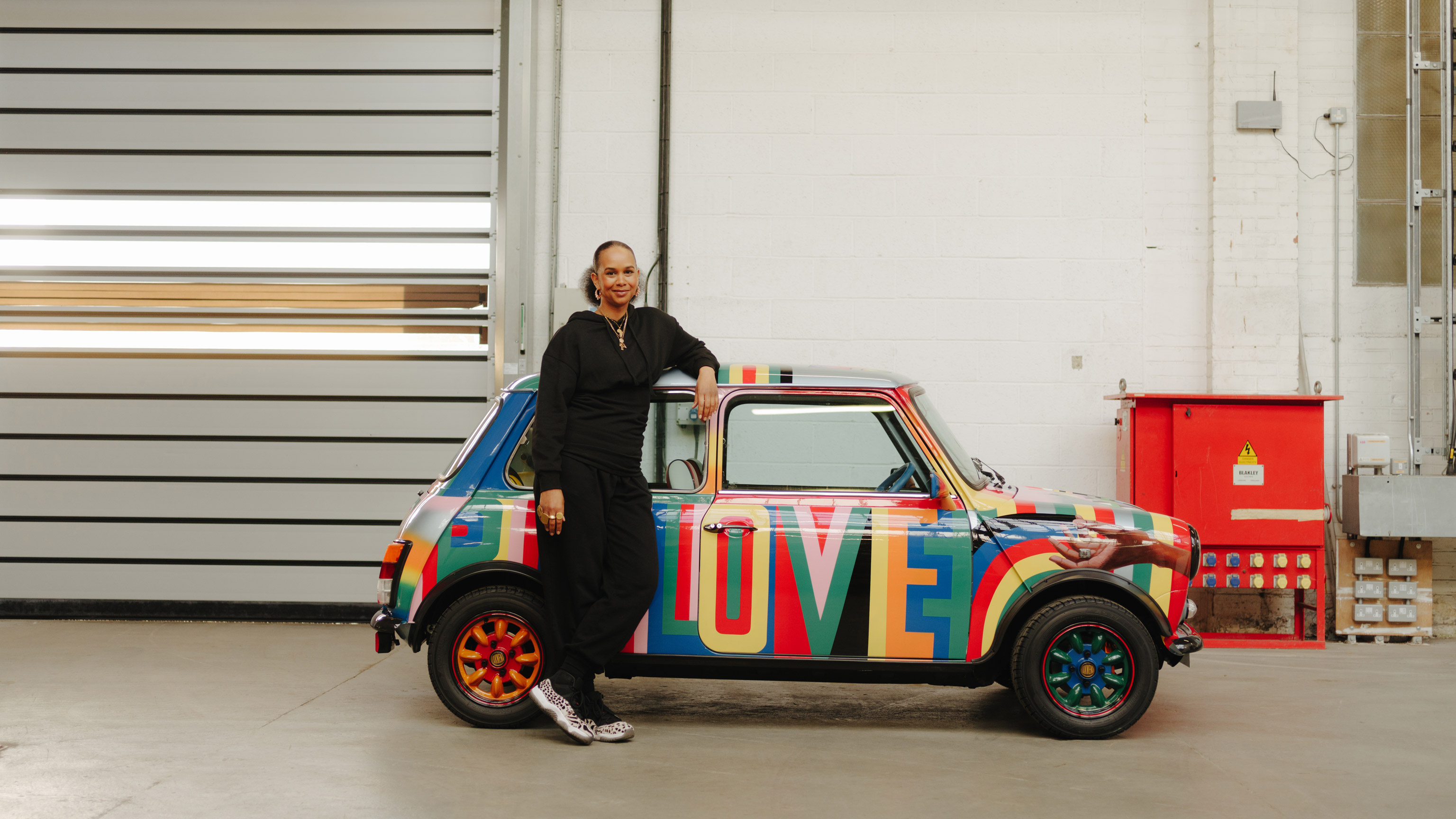 Lawena stands in front of her designed and colourful Mini classic. The side of the car reads “BIG LOVE”.
